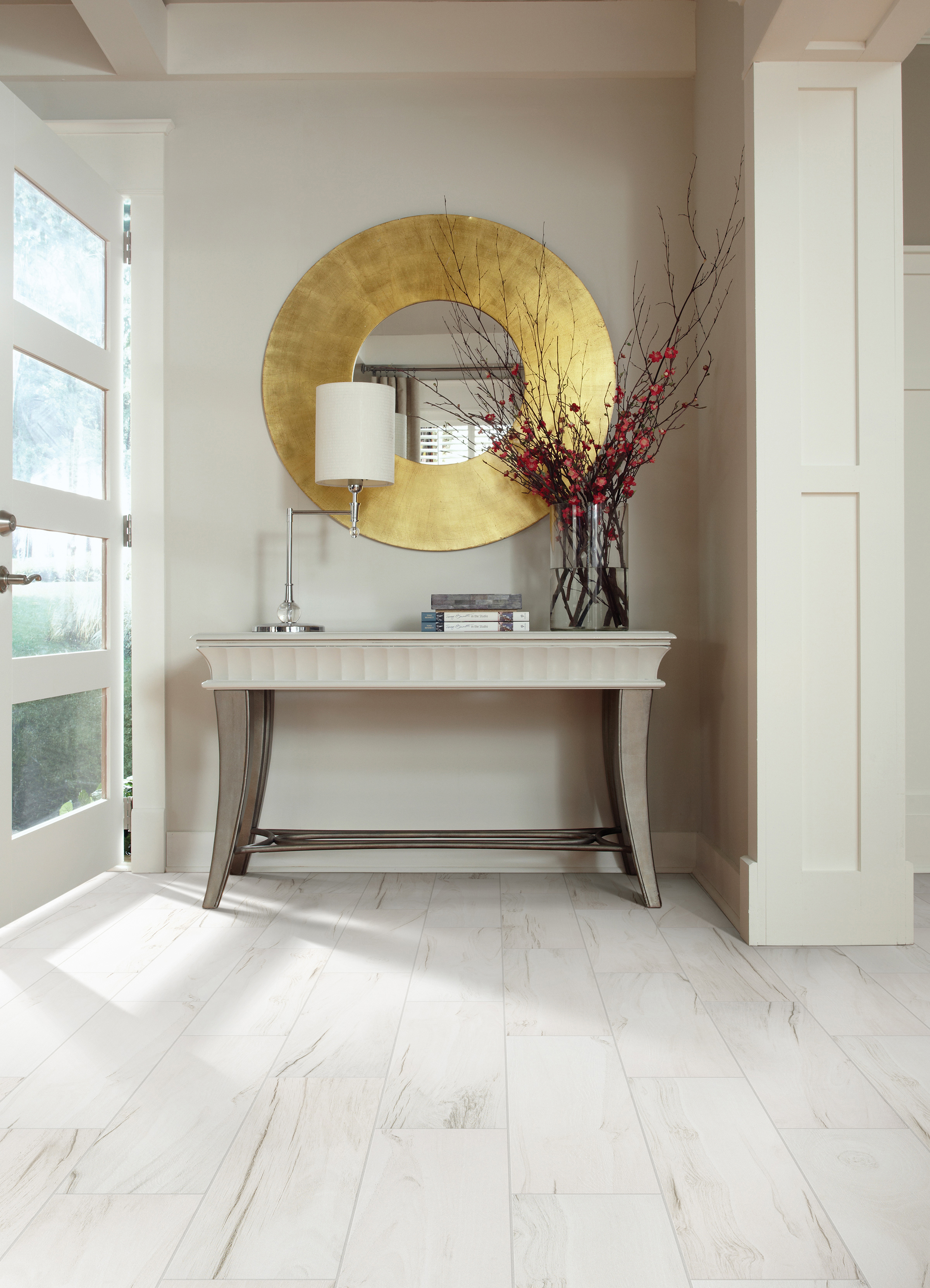 Hallway with tile flooring, table, golden mirror, and door leading to outside
